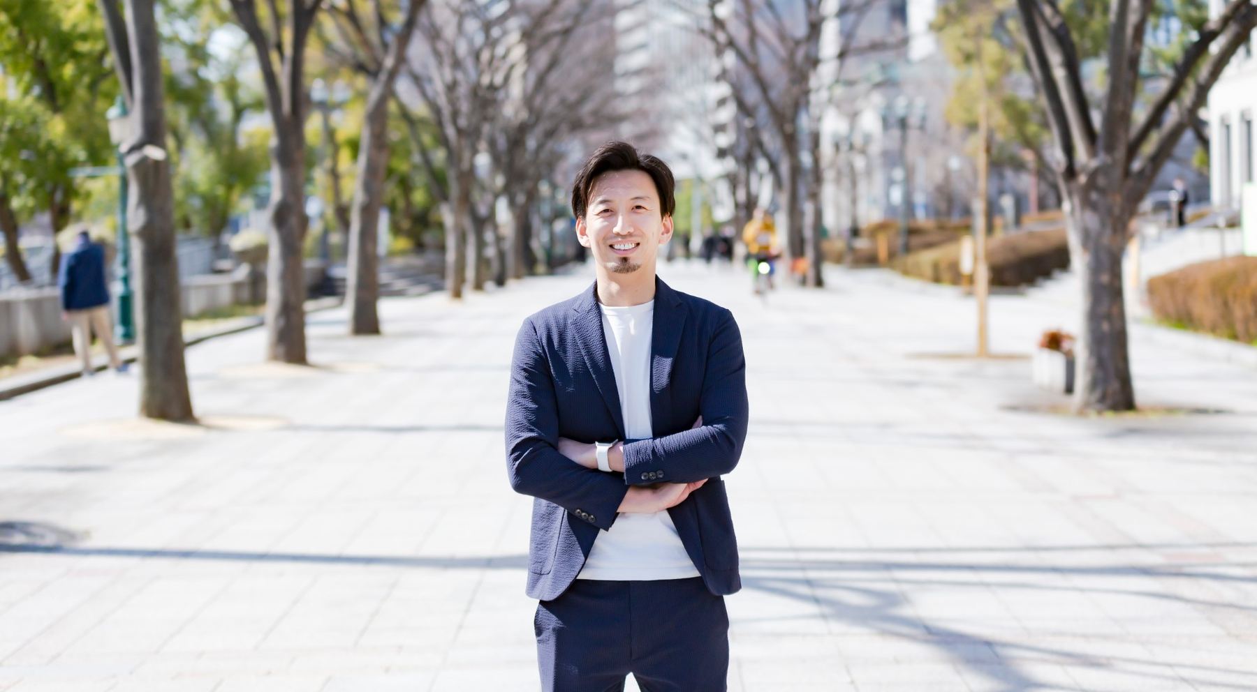 並木道で腕を組んで笑う、株式会社Smartaleck代表取締役の河井大志さん